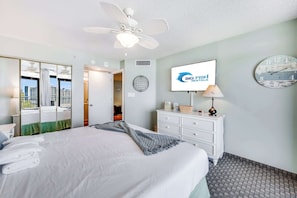Ein Hotelzimmer mit Bett, Deckenventilator, Fernseher, einer Uhr und Blick auf die Stadt.