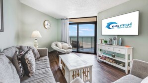 Un salon comprenant un canapé, un fauteuil, une table basse et un téléviseur fixé au mur.