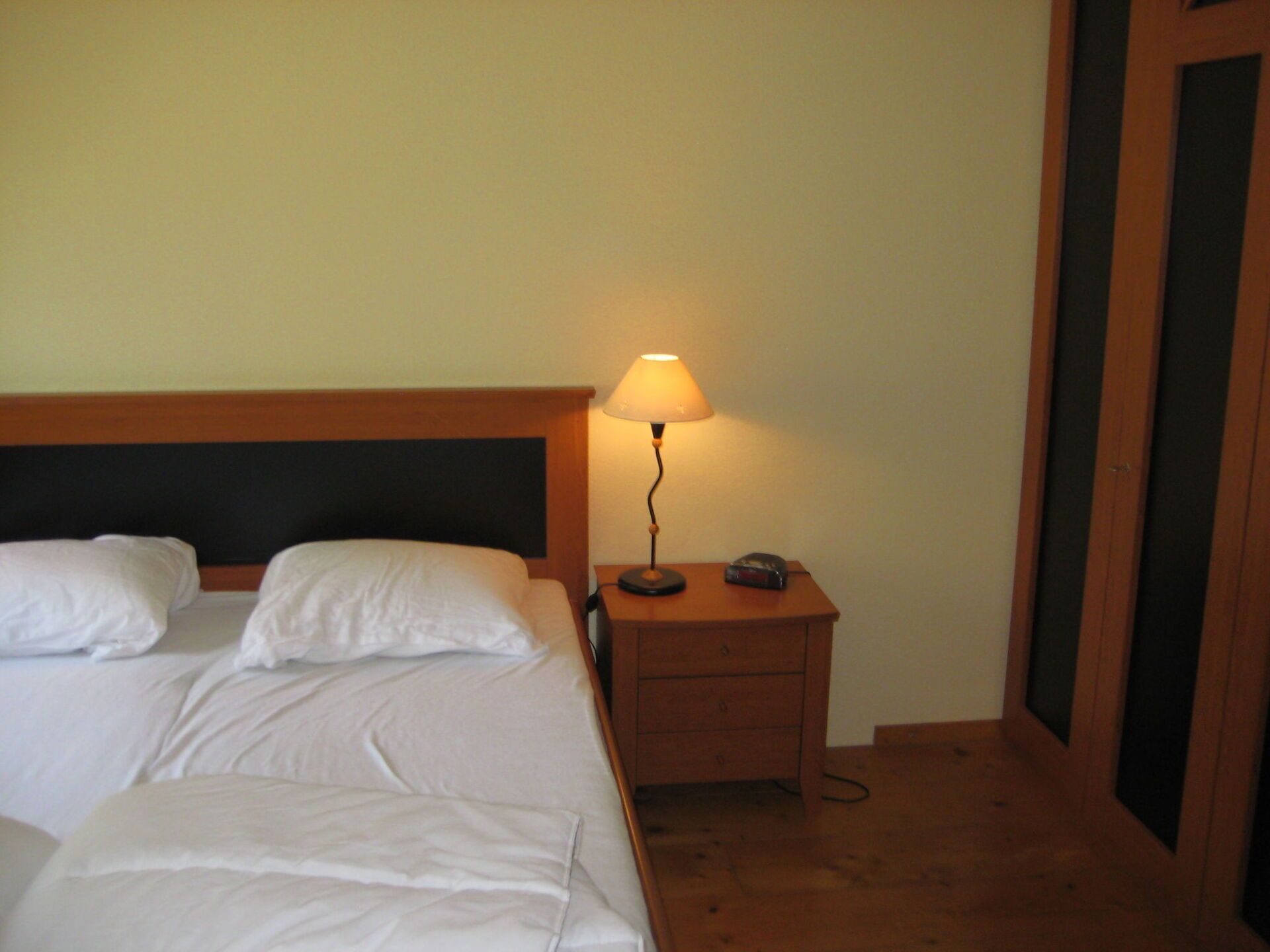 Hotellihuone, jossa on sänky, yöpöytä lampun kanssa ja puhelin.