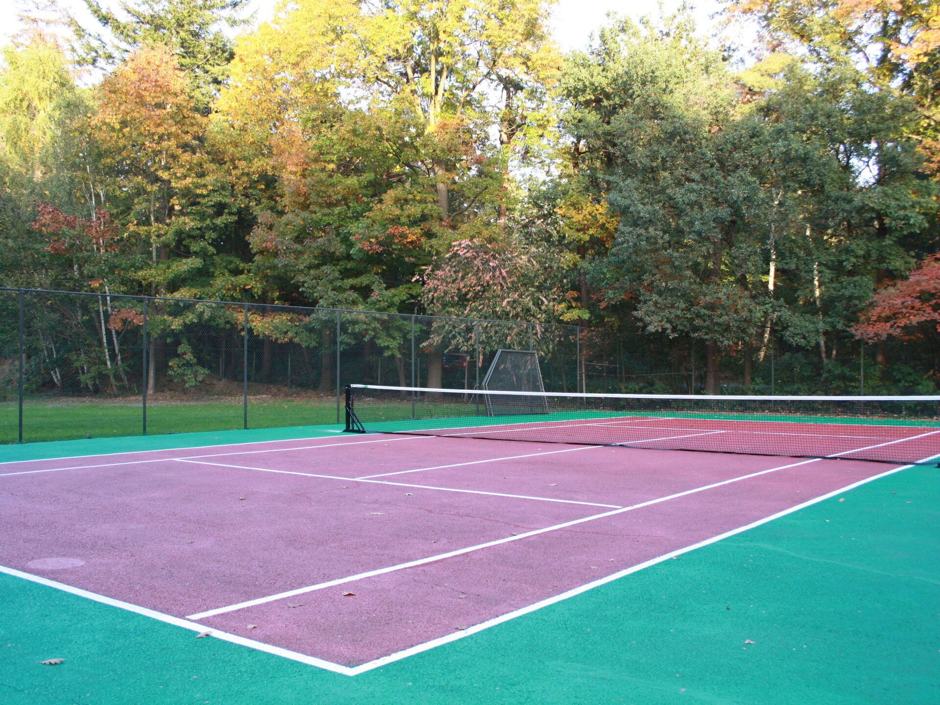 Ein Tennisplatz im Freien mit Netz, umgeben von Bäumen.