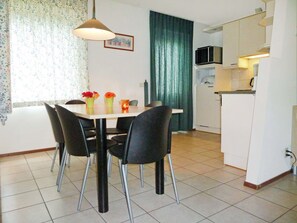 Een eetgedeelte met een tafel, stoelen en een hanglamp. Er is een keuken met een magnetron en een koelkast.