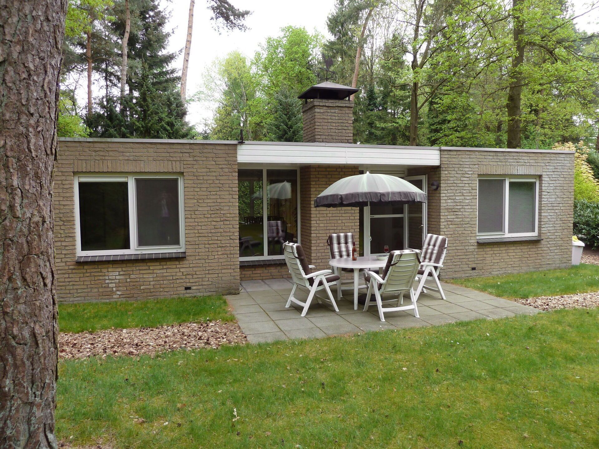 A patio with a table and chairs, a stone chimney, and a view of a forested area.