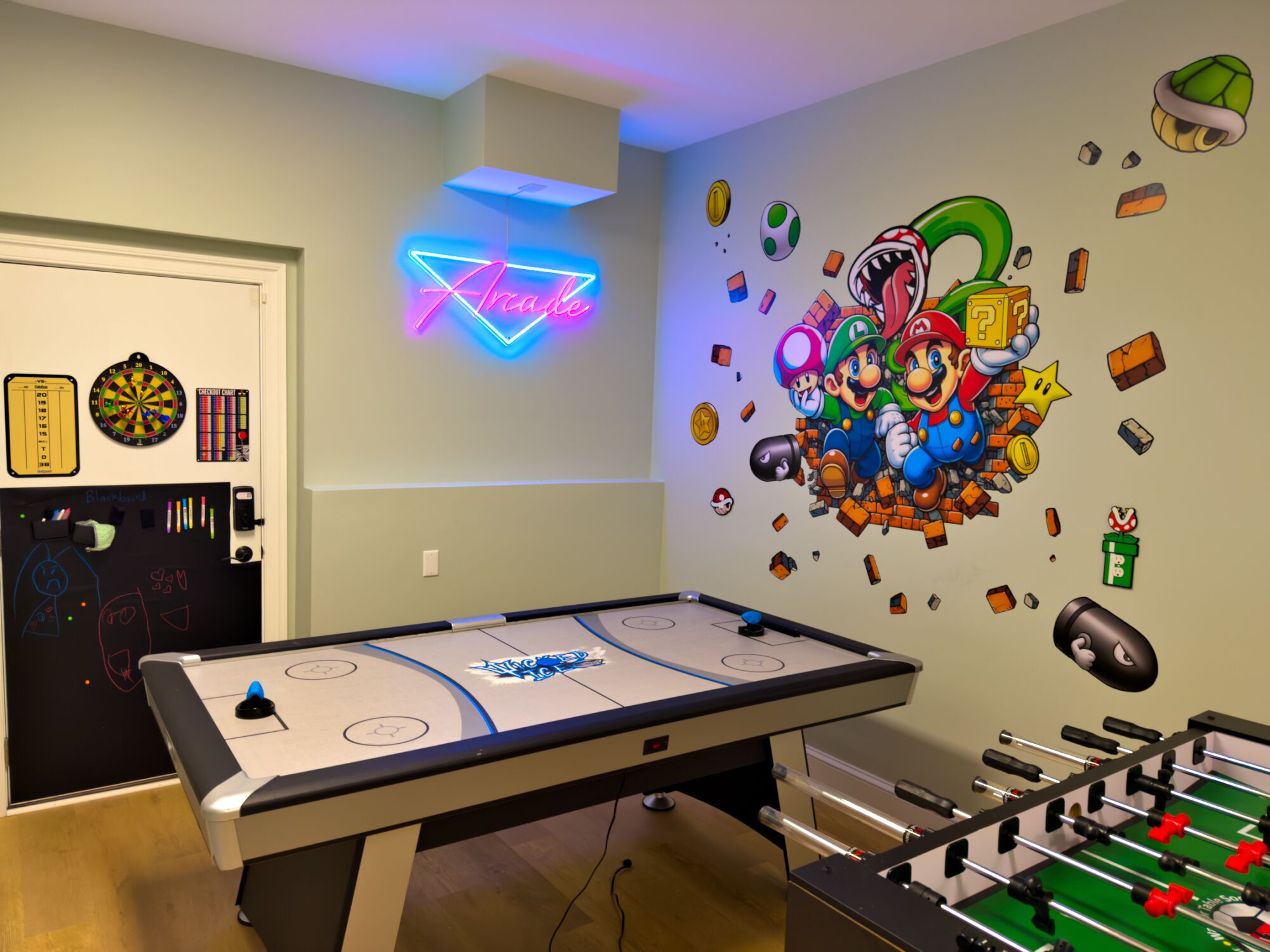 A room with a foosball table, a dartboard, and a neon sign.
