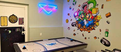 A room with a foosball table, a dartboard, and a neon sign.