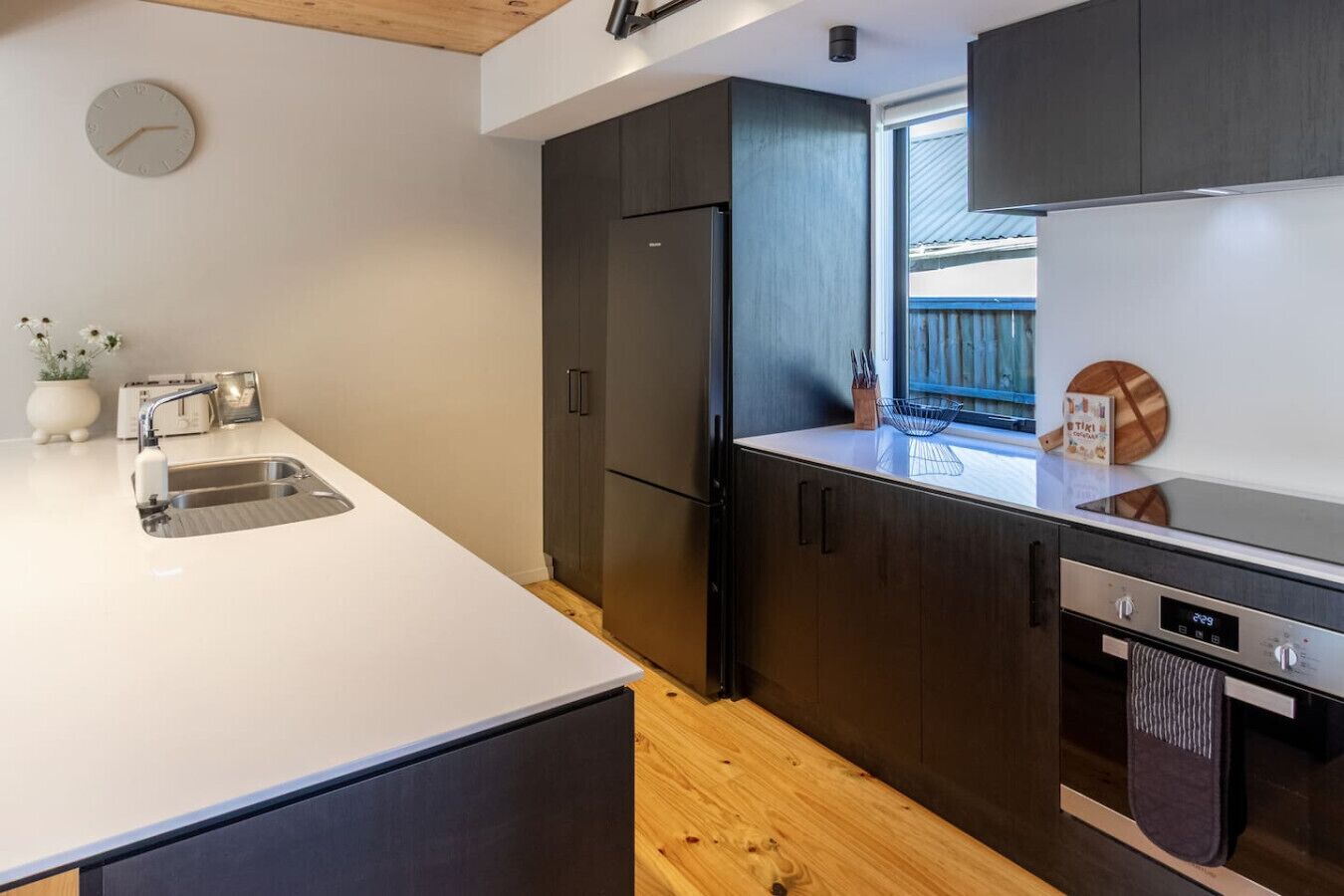 Una cocina moderna con encimera blanca, armarios oscuros, refrigerador de acero inoxidable y lavavajillas integrado.
