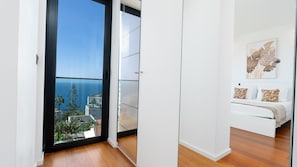 Ein modernes Schlafzimmer mit großem Fenster, einem Bett mit gemusterten Kissen und einem an der Wand hängenden Kunstwerk.