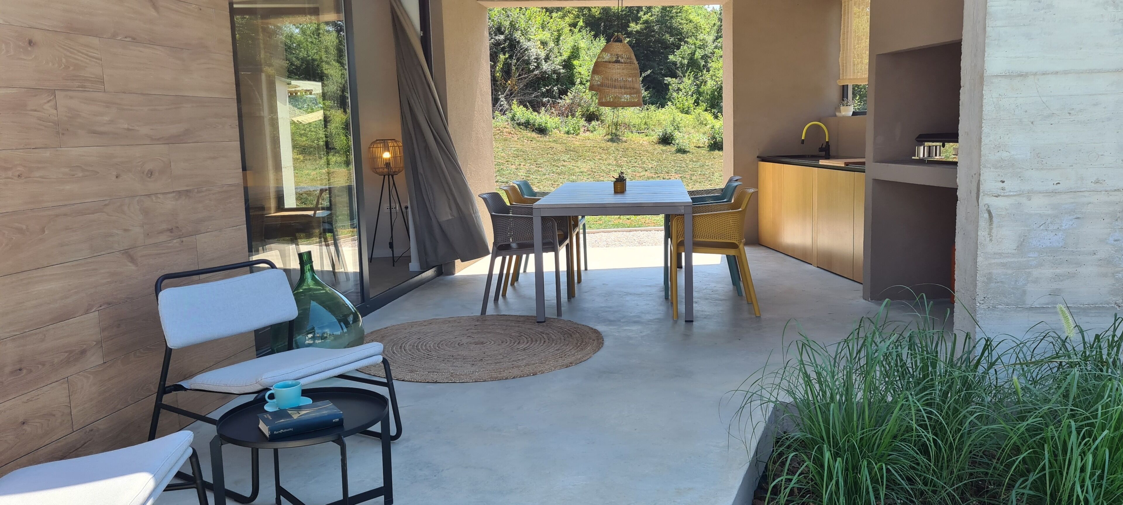 Un'area pranzo all'aperto moderna con tavolo e sedie, un piccolo tappeto rotondo e vista sul giardino.
