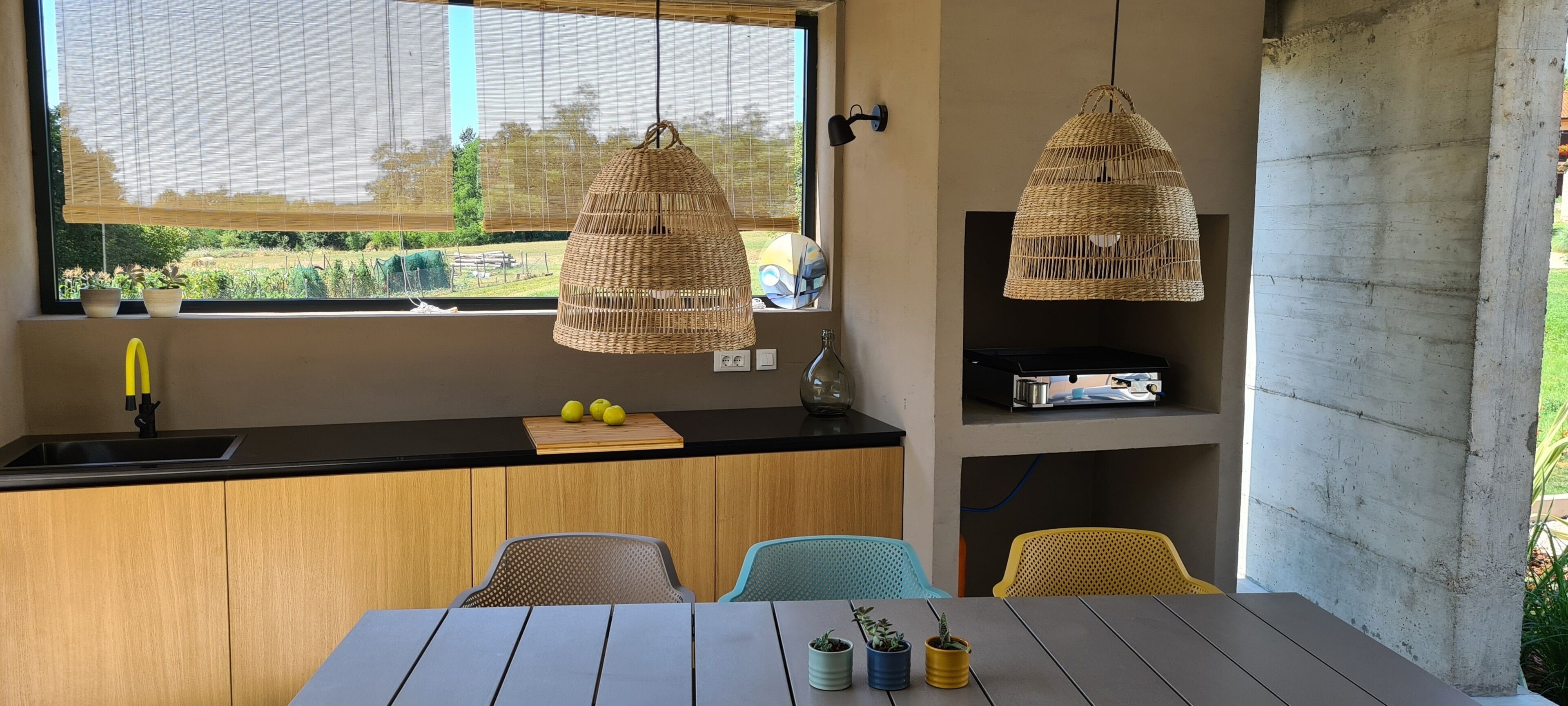 A modern kitchen with a large window, wooden cabinets, a black countertop, and a dining area with a table and chairs.