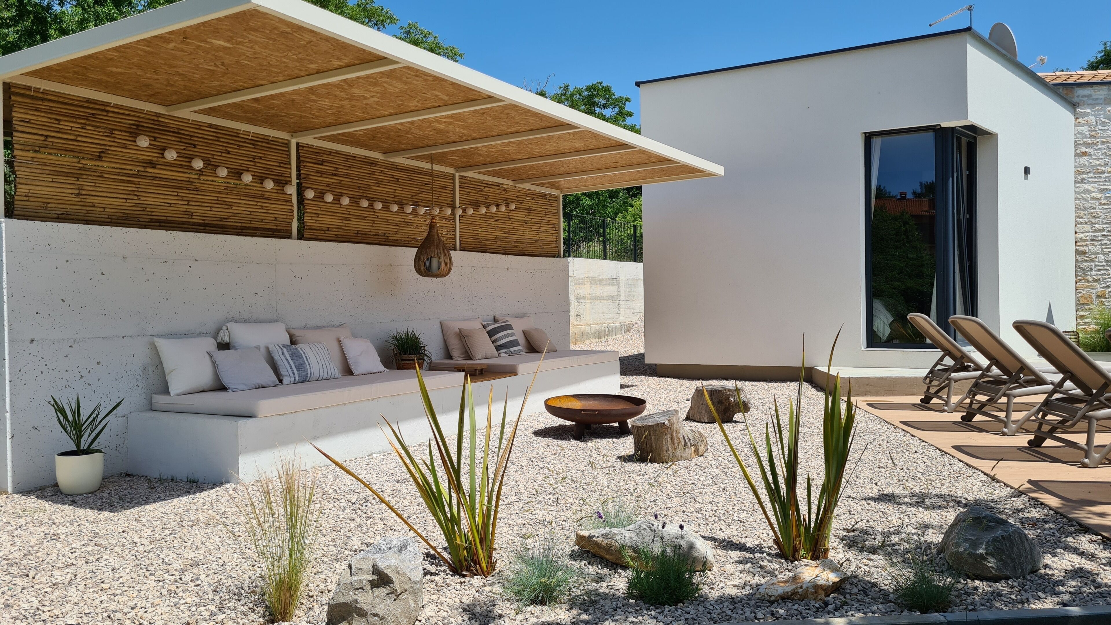 A modern outdoor seating area with a wooden ceiling, a stone wall, and a small pool.