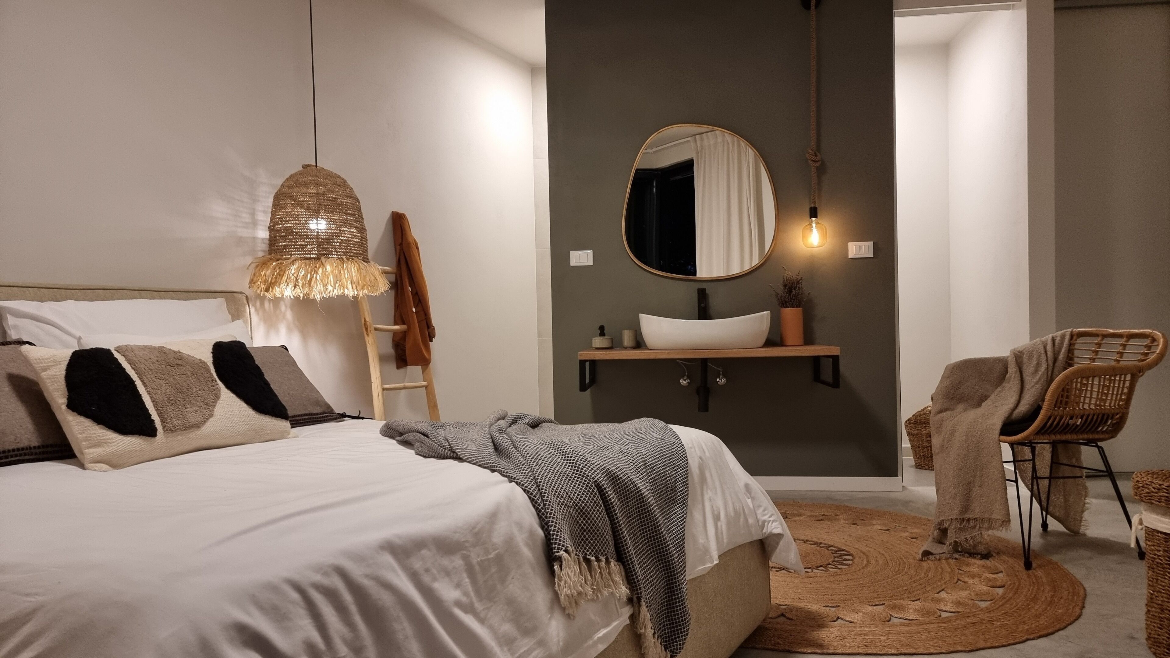 Una camera da letto con un letto, un comodino, uno specchio, una lampada a sospensione, una sedia e un tappeto.