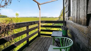 Una terraza de madera con vista a un campo verde, una mesa con una planta en maceta y una silla.