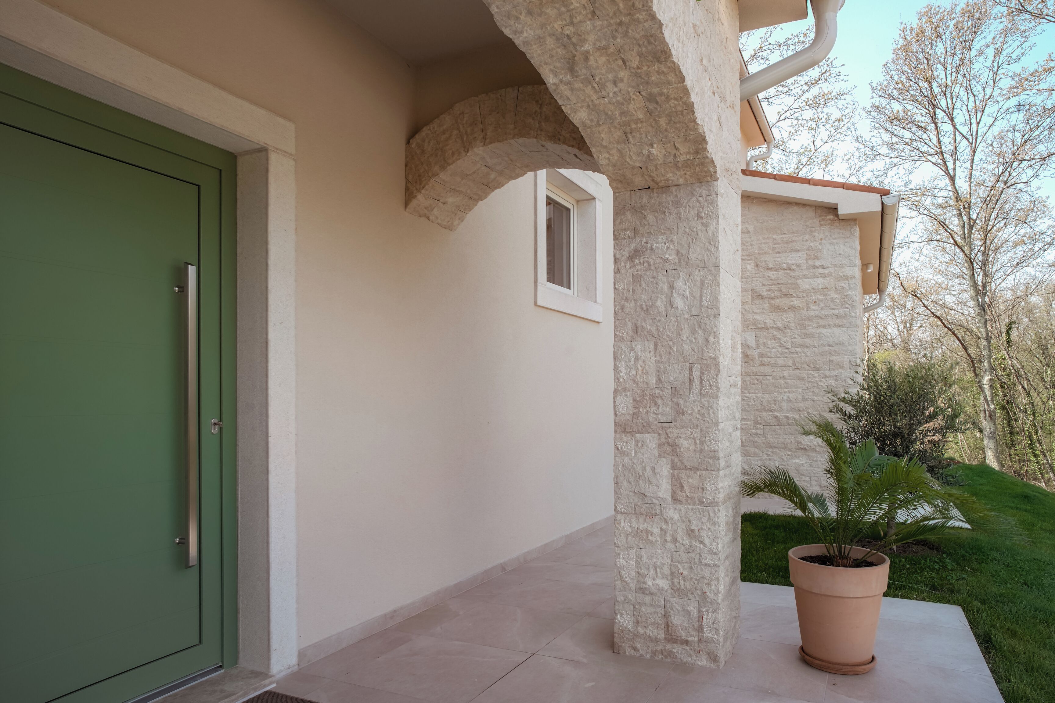 A building entrance with a green door, stone pillars, a window, and a potted plant.