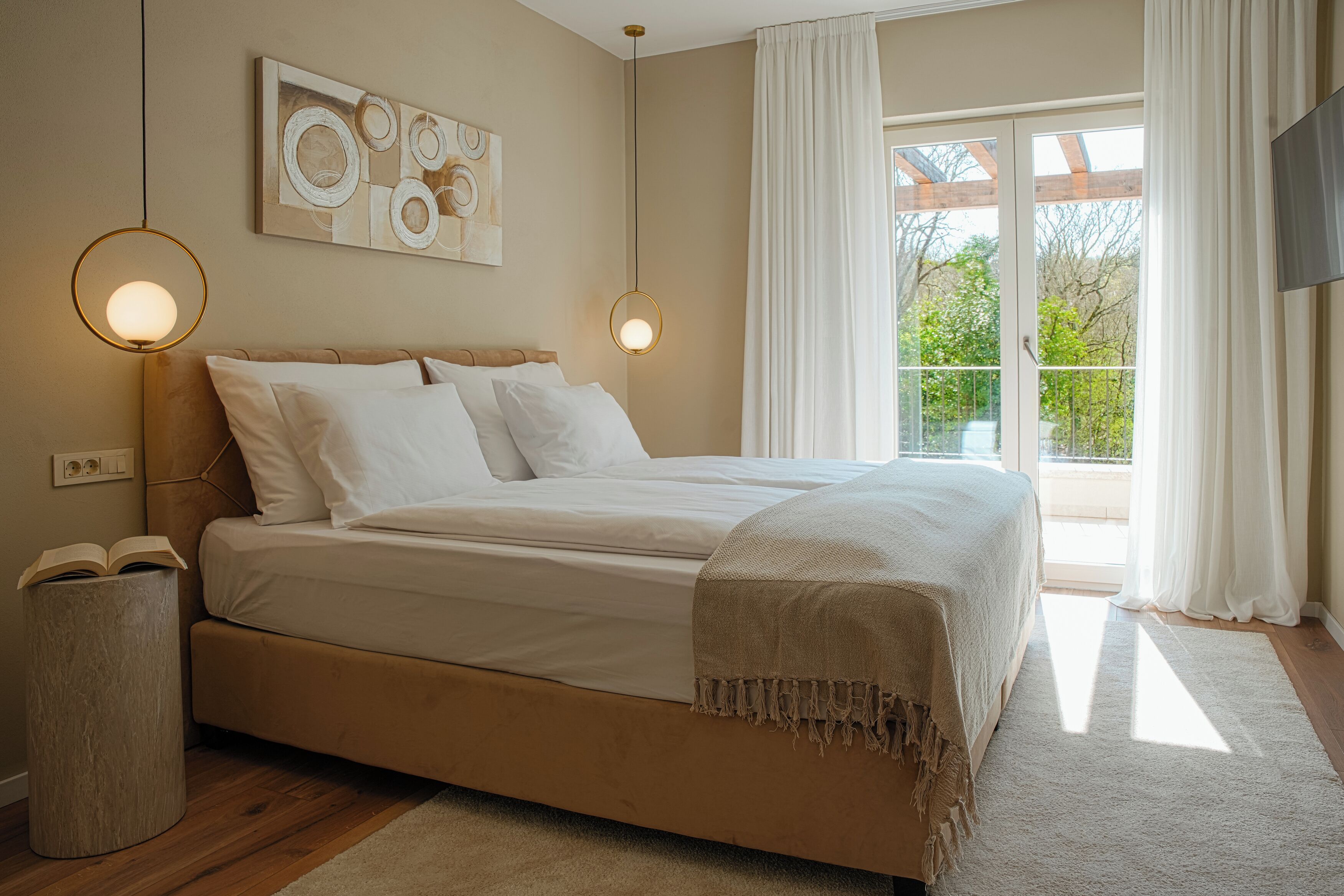 Ein Schlafzimmer mit Bett, Nachttischlampe, Überwurfdecke, einem Gemälde an der Wand und einem Fenster mit Vorhängen.