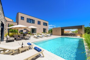 Ein modernes Hotel mit Schwimmbad, Sitzgelegenheiten im Freien und blauem Himmel.