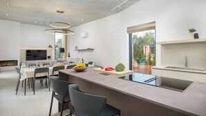A modern kitchen with a central island, dining area with chairs, and a large window providing a view of the outdoors. - Villa La Mari (Istria - Poreč) (Poreč)