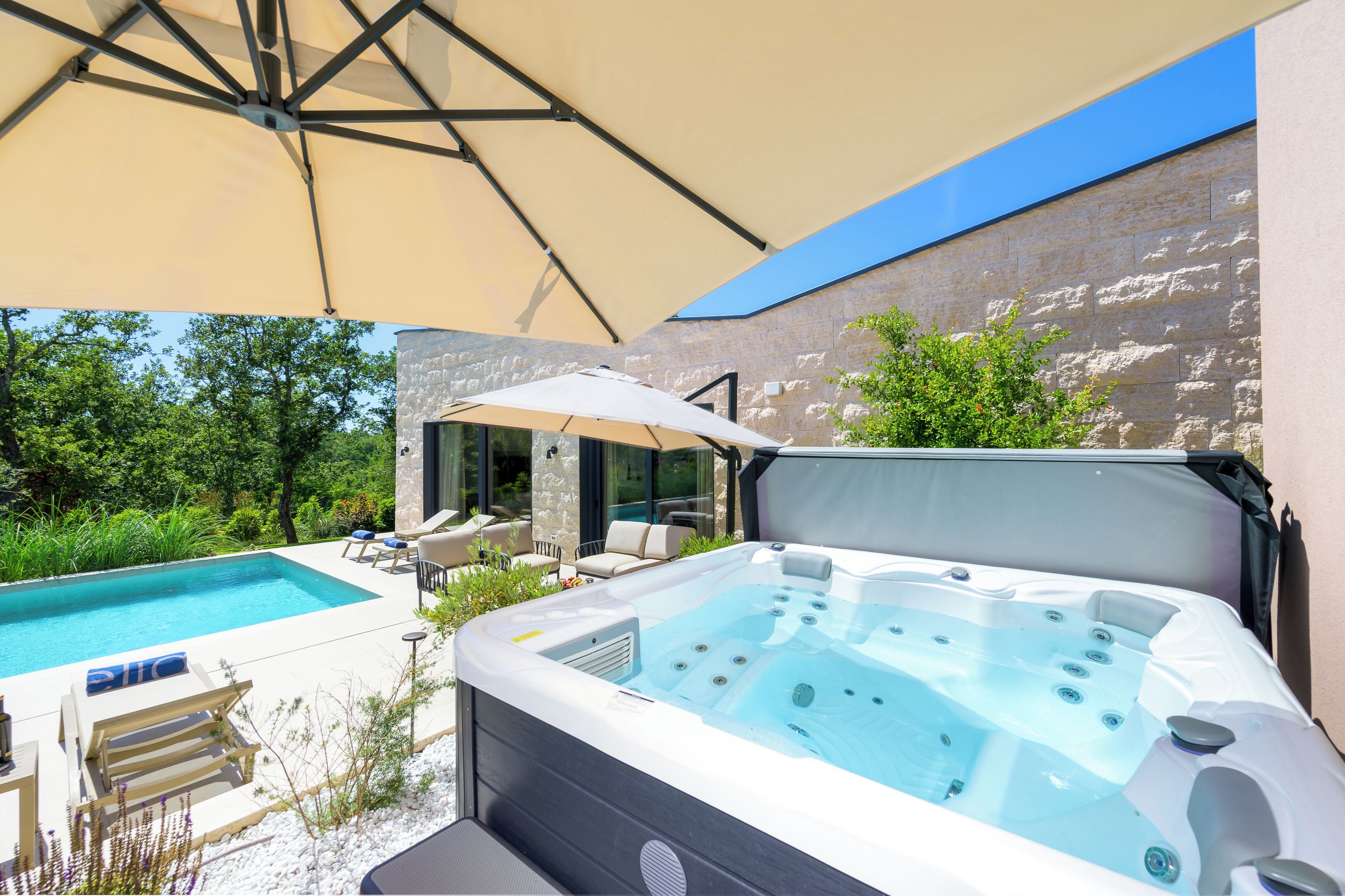 A hot tub with a view of a swimming pool and a stone wall.