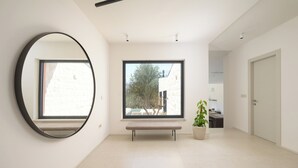 Un interior moderno con un espejo grande, un banco, una planta en maceta y vistas a través de un ventanal.