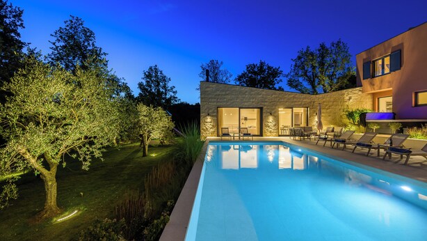 Un área moderna junto a la piscina, con una piscina cristalina, sillas de descanso y un edificio de piedra con amplias ventanas.