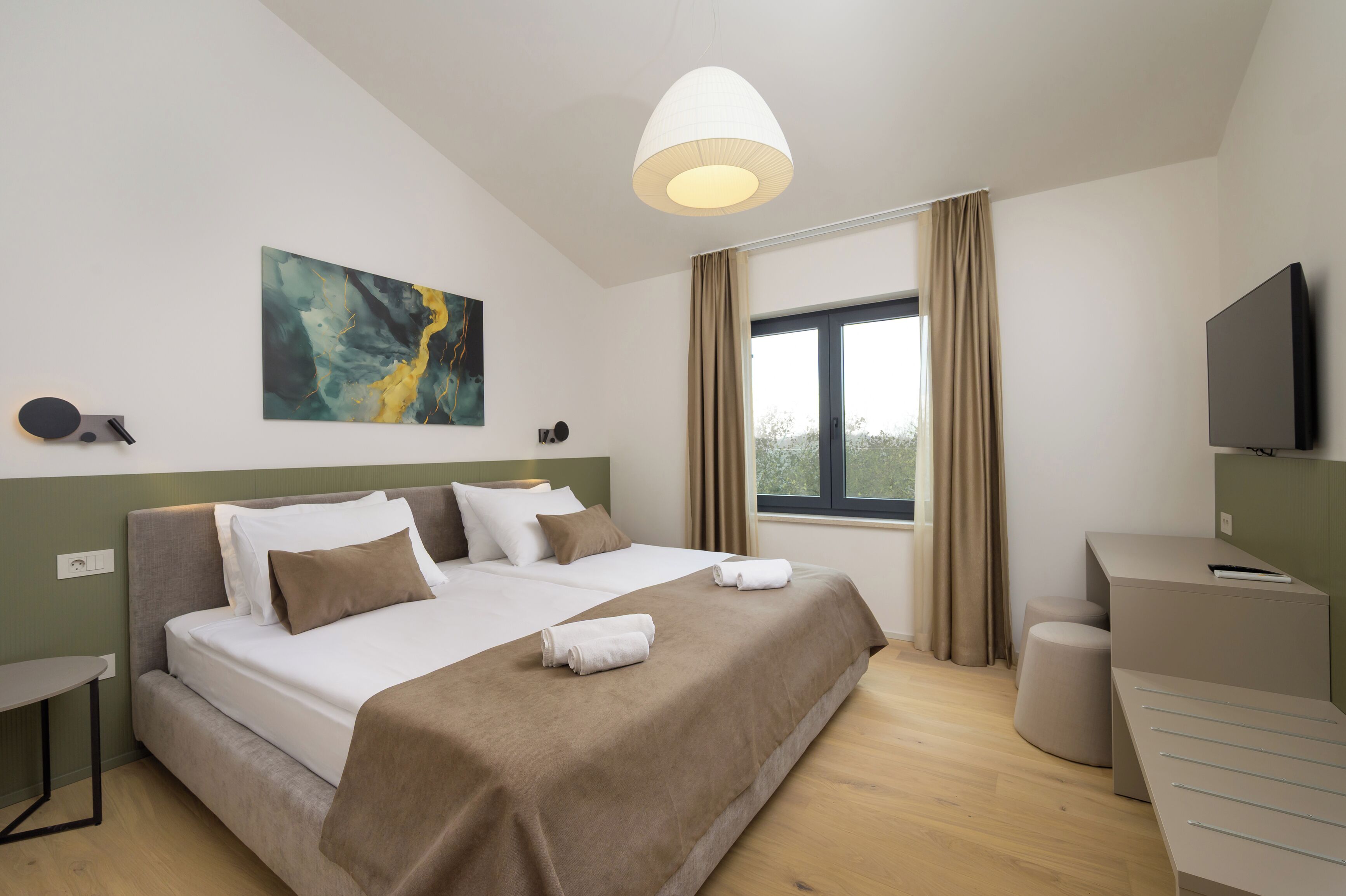 A modern hotel room with a large bed, a desk, a television, and a window with curtains.