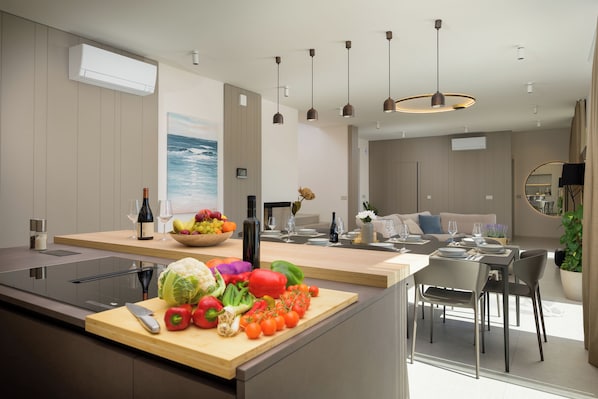 Une cuisine moderne avec un plan de travail en bois, une planche à découper avec des légumes et un coin repas comprenant une table et des chaises.