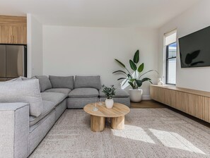 A modern living room with a sectional sofa, a round wooden coffee table, a potted plant, and a large window.