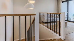 A staircase with wooden handrails and black balusters, leading to a balcony with a sofa and a table. - Black Wattle Beach House (Casuarina)
