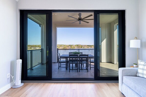 Une pièce dotée d’une porte-fenêtre coulissante donnant sur un balcon extérieur, avec une table et des chaises, un ventilateur de plafond et un lampadaire.