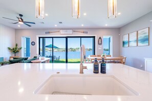 Une cuisine moderne dotée d’un grand îlot central, d’un coin repas offrant une vue sur un lac et d’un ventilateur de plafond.