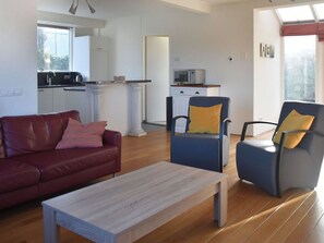 Ein Wohnzimmer mit einer Couch, einem Couchtisch und zwei Sesseln. Es gibt eine Küchenzeile mit Kühlschrank, Mikrowelle und Schränken.
