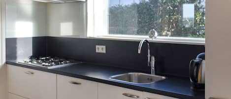 A modern kitchen with a gas stove, stainless steel sink, and a window with a view of greenery.