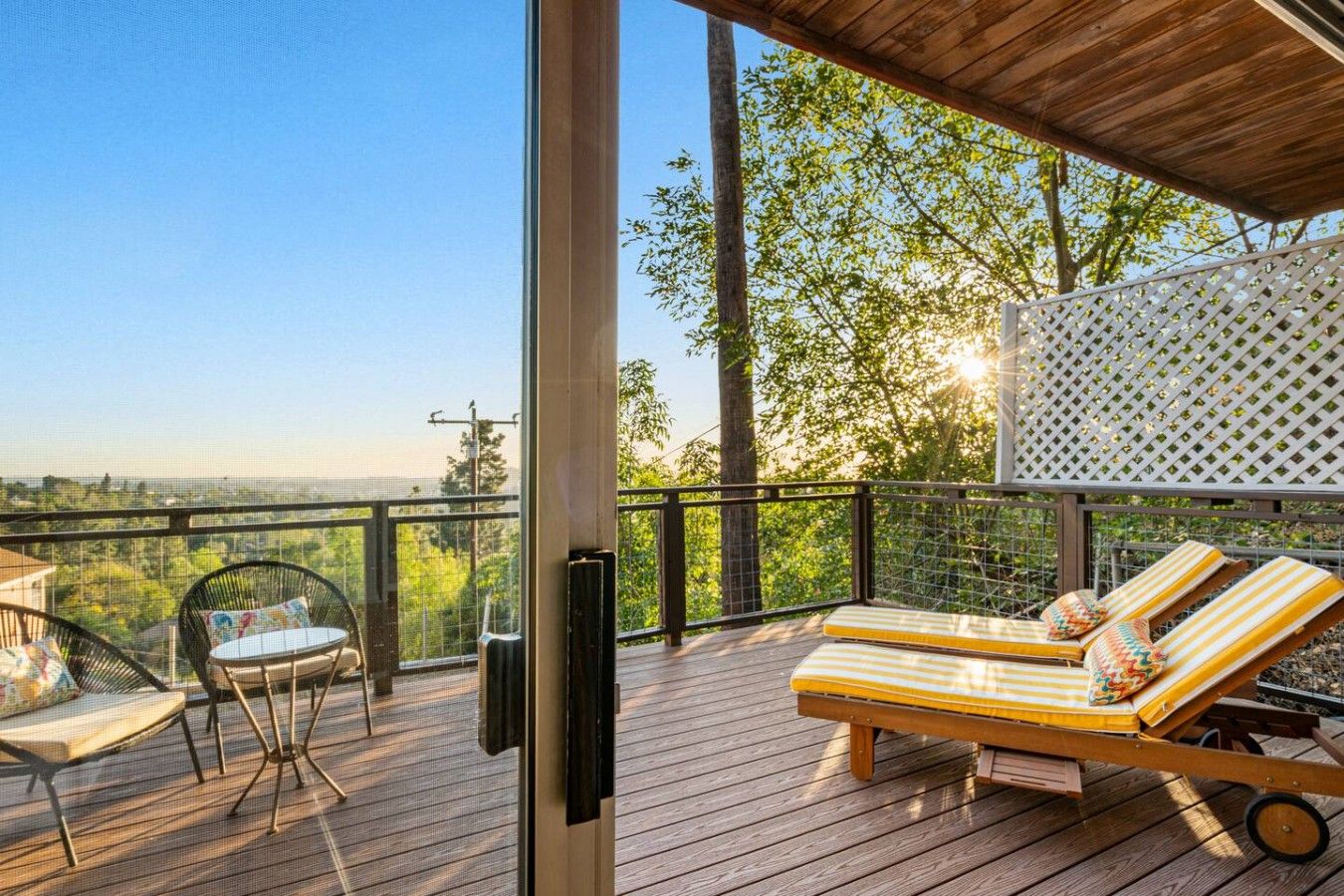 A wooden deck with two lounge chairs and a table, overlooking a scenic landscape.
