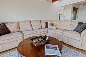 A living room with a beige sectional sofa, a wooden coffee table, and a visitor's guide on the table. - Panoramic Ocean View Retreat - Family Friendly (La Mesa)