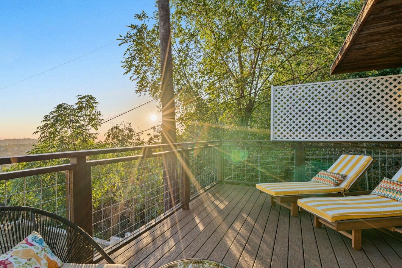 Eine Holzterrasse mit Geländer, zwei Liegestühle mit Streifenpolstern und ein Gitterzaun.