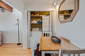 A compact kitchen with a built-in washing machine, a dining table with chairs, and a mirror on the wall. - Panoramic Ocean View Retreat - Family Friendly (La Mesa)