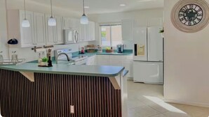Uma cozinha moderna com armários brancos, uma ilha central, iluminação pendente e um relógio de parede.