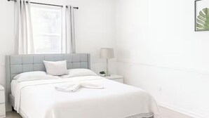 Quarto com cama, mesas de cabeceira, ventoinha no teto e janela com cortinas.