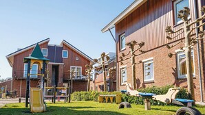 Een speeltuin met een glijbaan en schommels, naast een gebouw met een bakstenen gevel en een groen dak.