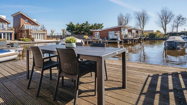 Een pand aan het water met een eetruimte, boten en moderne huizen.