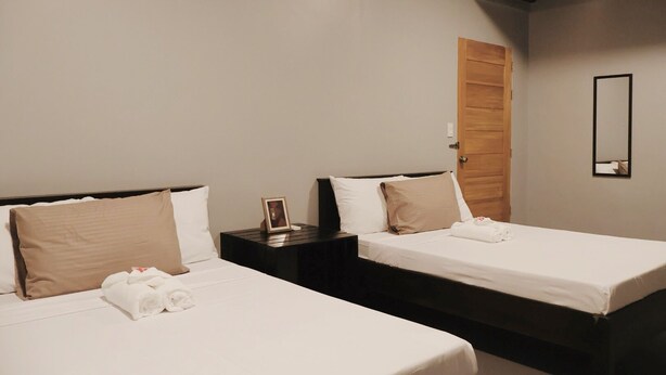 A hotel room with two beds, a wooden door, a small bedside table with a picture frame, and a mirror on the wall. - Roccia Transient  (San Fernando)