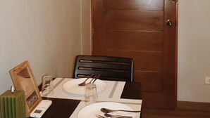 A dining table set with plates, cutlery, and a glass, with a framed picture on the wall and a wooden door in the background. - Roccia Transient  (San Fernando)
