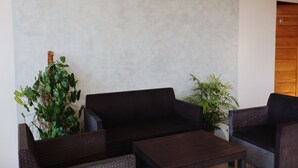 A room with a dark wicker sofa, a small wooden table, and two potted plants. - Roccia Transient  (San Fernando)