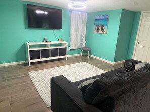 Ein Wohnzimmer mit türkisfarbenen Wänden, einem Flachbildfernseher, einer weißen Unterhaltungsanlage, einem grauen Sofa und einem gemusterten Teppich.
