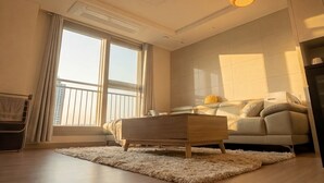 Un salon moderne avec un canapé, une table basse en bois et une grande fenêtre agrémentée de rideaux.