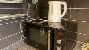 Une cuisine moderne avec un four à micro-ondes noir, une machine à café blanche et une horloge numérique affichant 12 h 08.