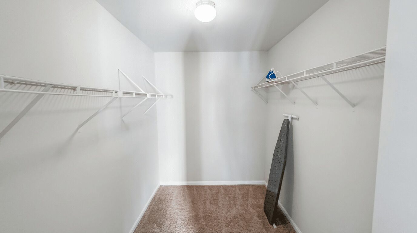 A narrow hallway with white walls, a brown carpet, and white shelving units with hanging clothes.