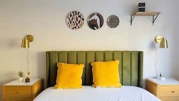 A bedroom with a green upholstered headboard, two yellow pillows, a white bedspread, and a bedside table with a lamp.
