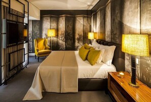 A modern bedroom with a large bed, two bedside lamps, a chair, and a TV.