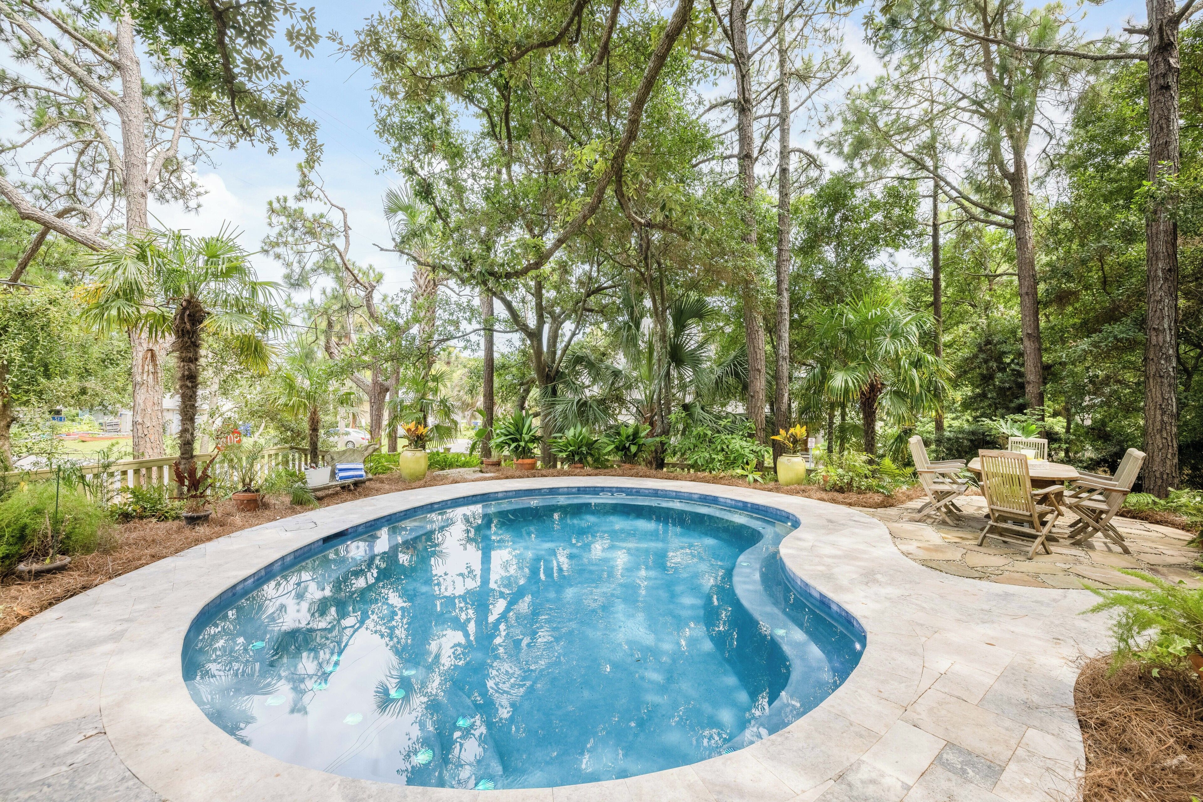 Ein von Bäumen umgebener Pool mit Terrasse und Gartenmöbeln.