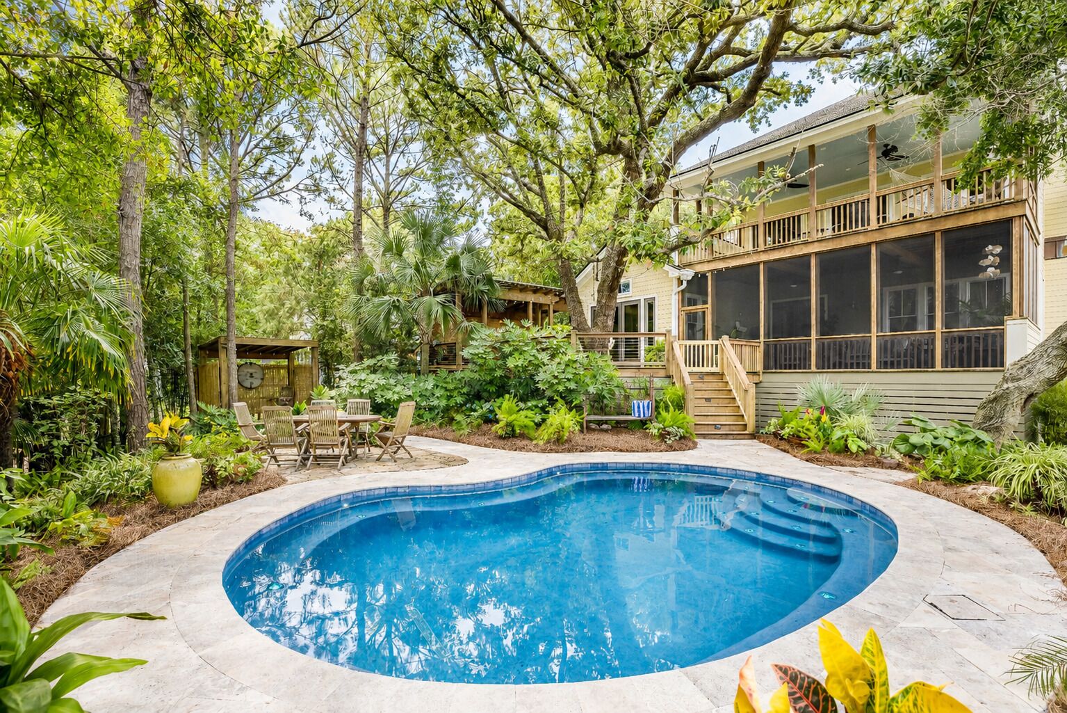 A backyard with a swimming pool, wooden deck, and lush greenery.