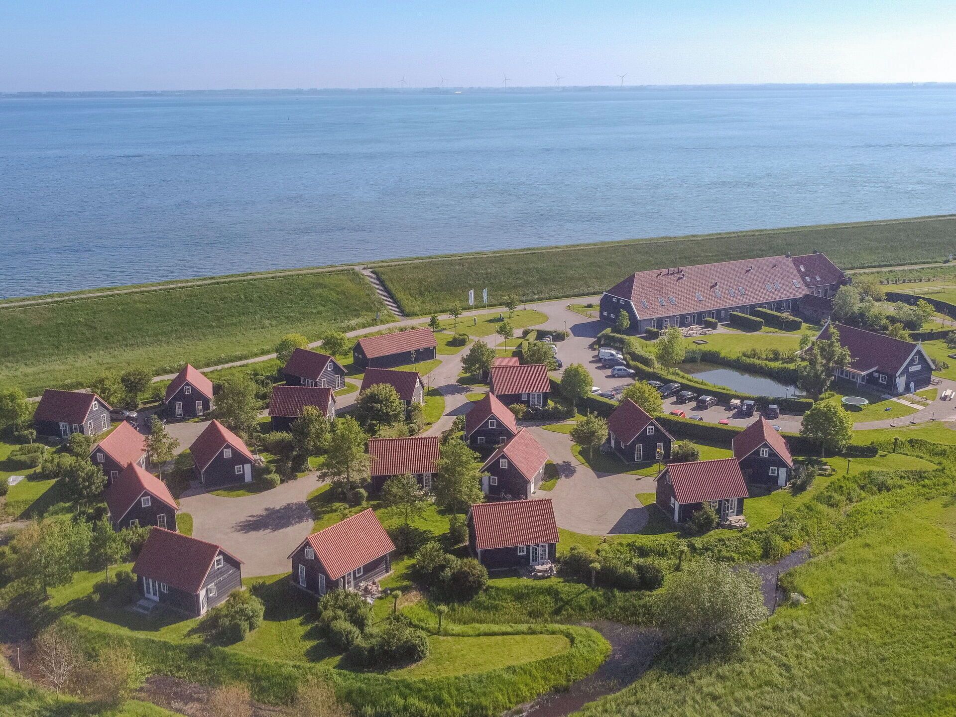 An aerial view of a coastal village with houses, a large barn, and a small lake.